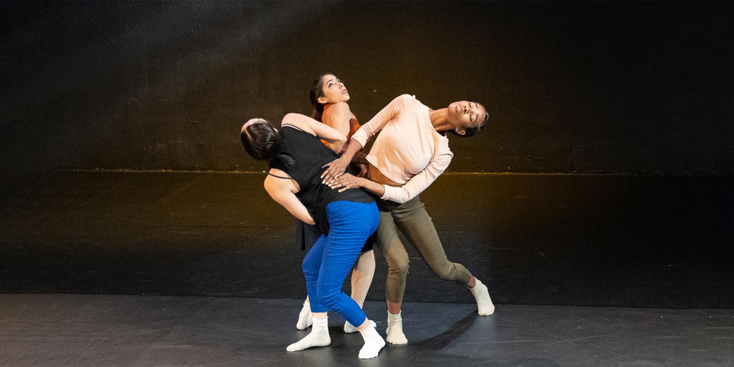Three people dance together on a dark stage.