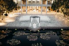 The courtyard set up for a wedding ceremony. White chairs are set in front of a simple, black chuppah