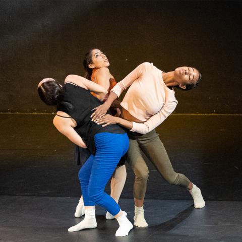 Three people dance together on a dark stage.