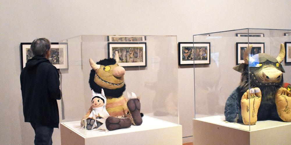 A stuffed monster and child in a monster costume in a case with a vitrine over them in a gallery setting.