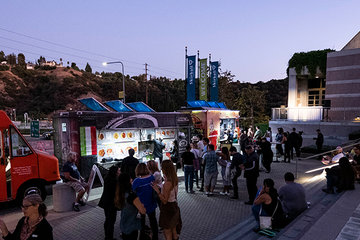 Photo of the front steps of the Skirball. People are standing around talking and ordering food from parked trucks. The words &quot;Late Night!&quot; are projected in lights on the side of the building.