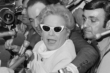 Black and white photograph of Martha Mitchell surrounded by journalists, cameras, and microphones.