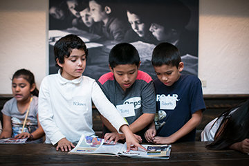 A group of students stand over a book in the Visions and Values gallery