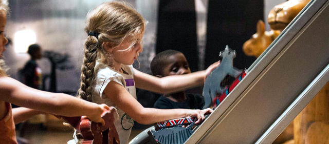 Two boys and a man watching animals go up a conveyer belt