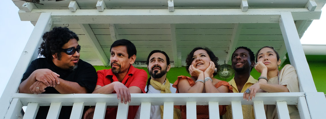 Six musicians smiling while looking over balcony railing