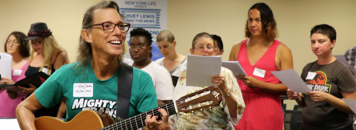 Person leading a group of singers while playing the guitar