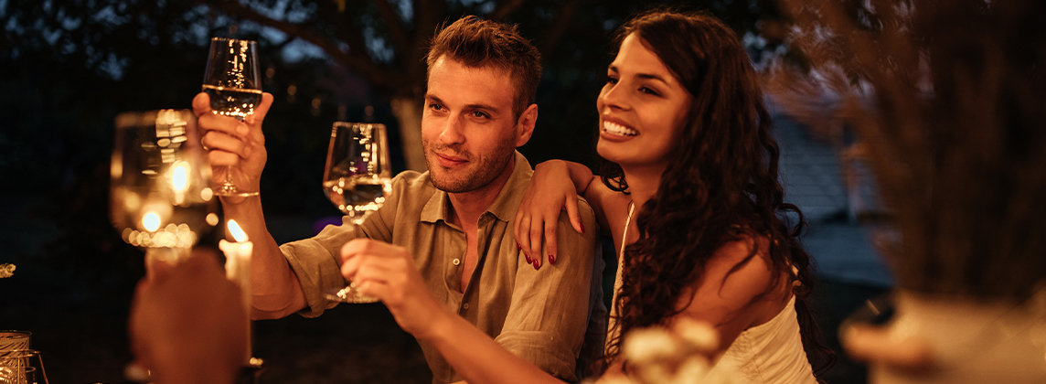 A couple holding their drinks in a toast at a festive outdoor table