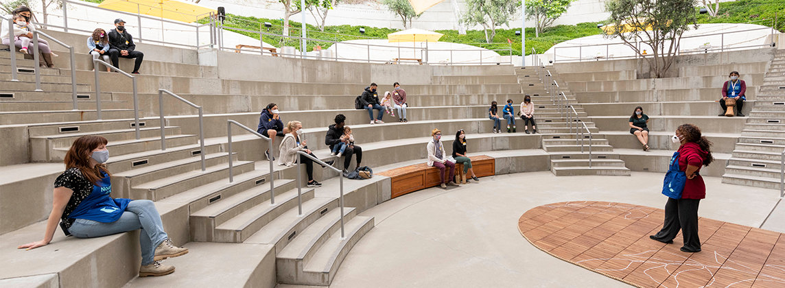 Photo of a group sitting distanced in an outdoor amphitheater watching someone speaking