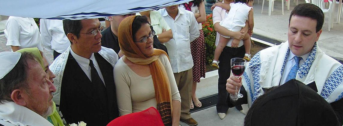 A rabbi holding up a wine glass surrounded by other people at a ceremony