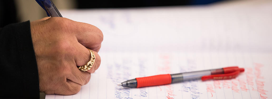 Close-up of hand writing with a blue pen and a red pen lying on a piece of paper