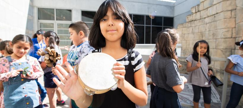 Girl holding tamborine with other girls and boys behind her