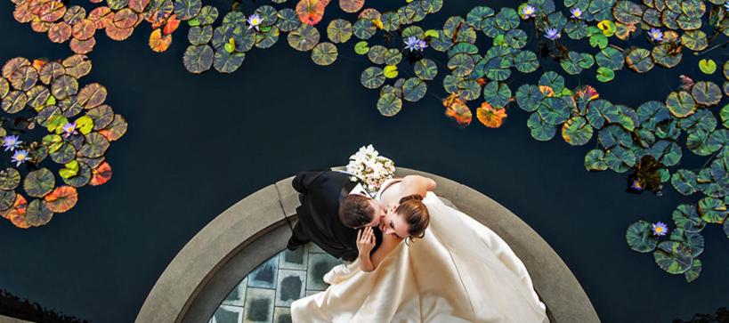 A bride and groom dancing next to a pond filled with water lillies