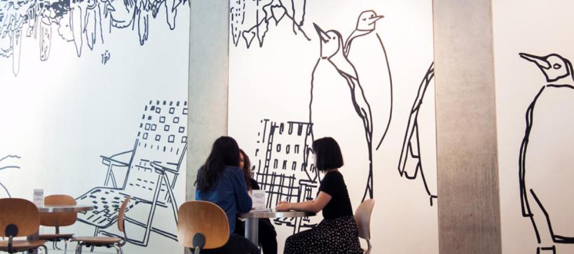 black and whilte drawings on wall with 3 people seated at a small table in front of it