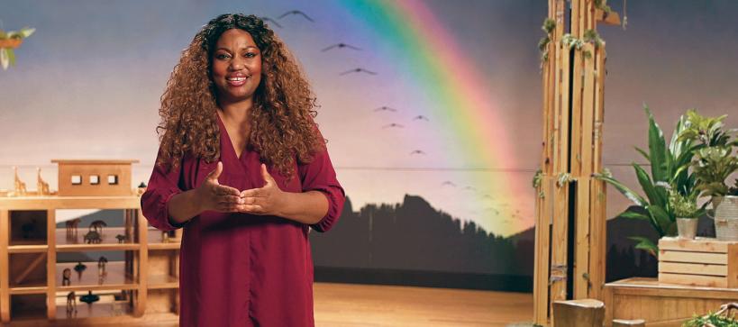 Educator smiling and standing in Noah's Ark exhibition with rainbow in the background 