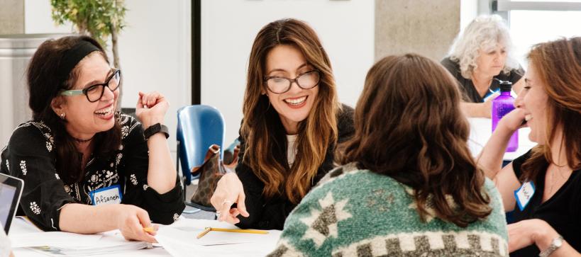 Four women sitting around a table in a class talking to one another