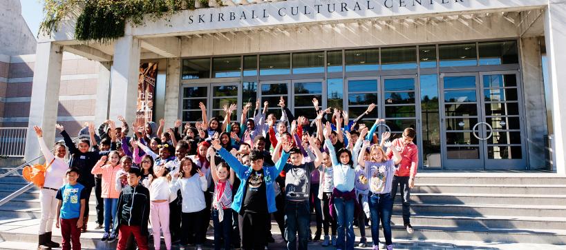 A group of school children on the front steps of the Skirball Cultural Center with arm raised up enthusiastically
