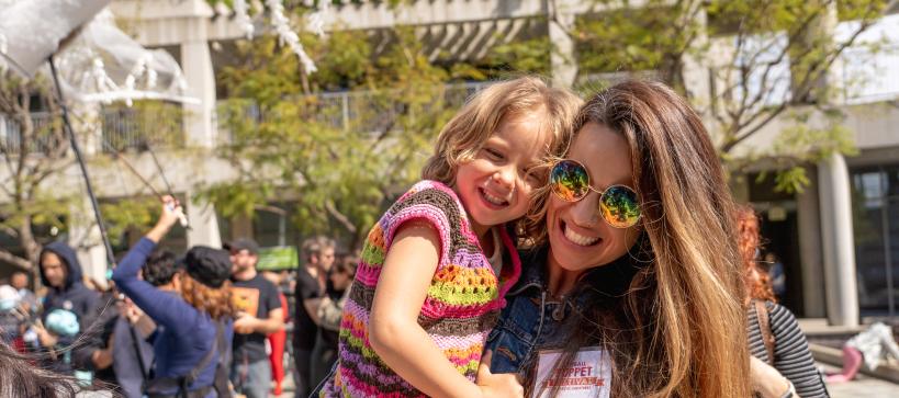 Mother holding young daughter dancing and smiling outside during a festival