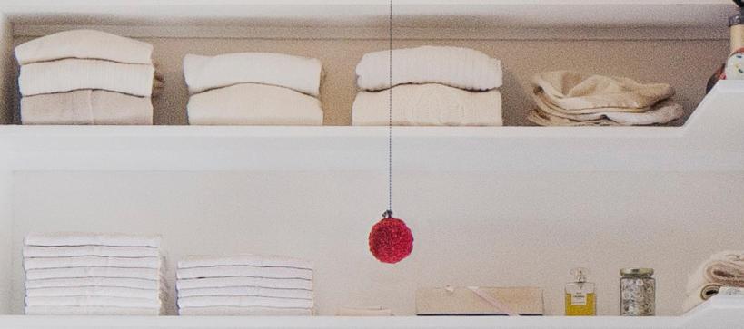 towels, perfume bottles and other items neatly arranged on shelves in a closet with a red ornament hanging on a string in front of them