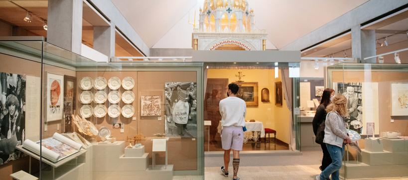 A few people walking a round a bright gallery with objects in cases and graphics on the walls.