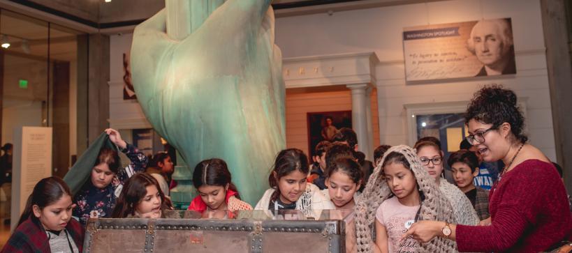 A docent pointing out features in a travel trunk to school children.