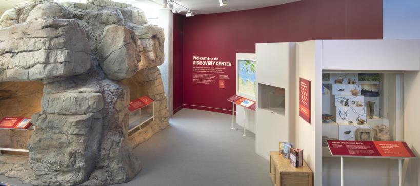 Photo of a artifact gallery with cases and a large rock ancient tomb with a big text wall that reads Discovery Center