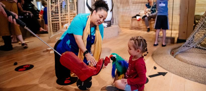 An educator kneels next to a young child playing engaging with animal puppets in the Ark