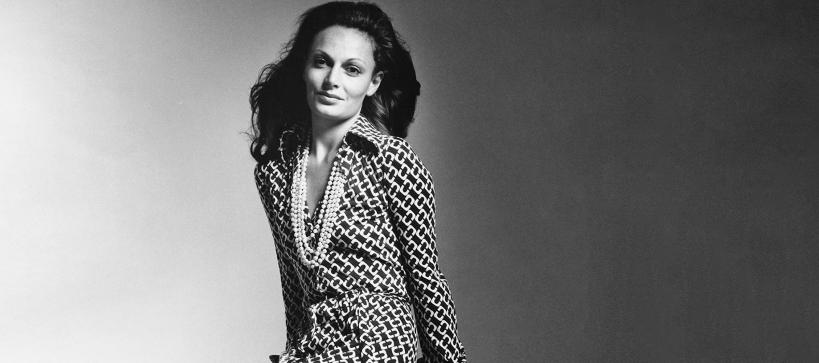 Black and white portrait of Diane von Furstenberg posing in her famous wrap dress smiling at the camera.