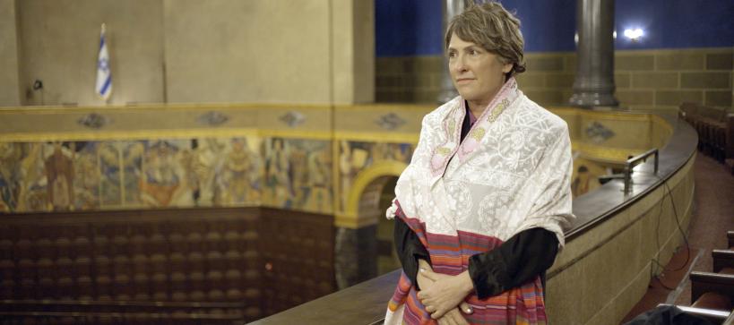 A person wearing a prayer shawl stands with hands clasped