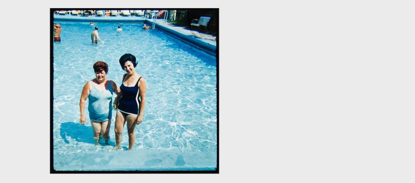 Two women standing in a shallow pool posing for a photo during the mid-century.