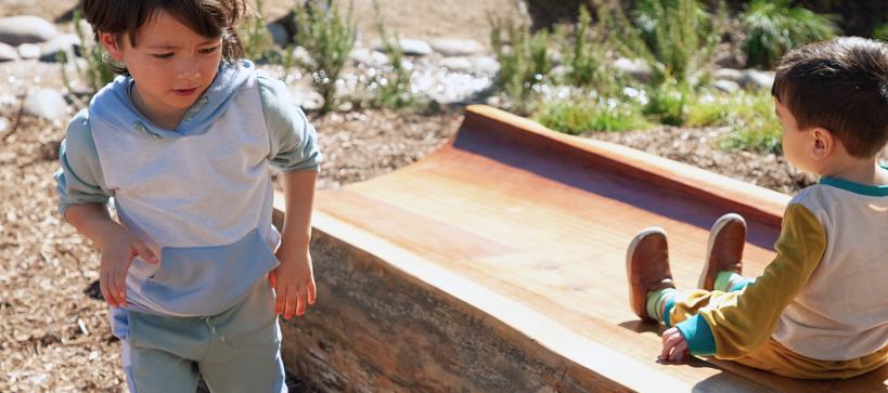 Two kids play outside in a garden.