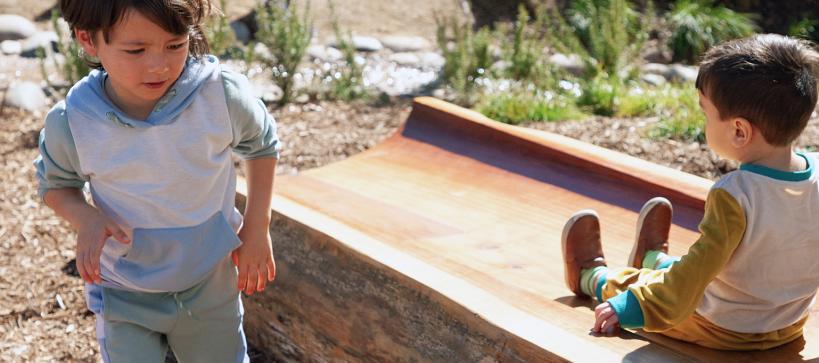 Two kids play outside in a garden.