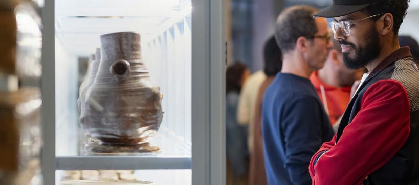 A man looks at pottery in a gallery case.