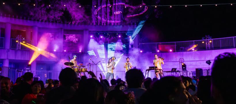 A band plays on an outdoor stage with dramatic lighting.