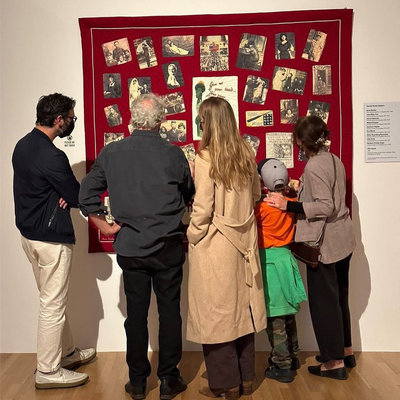 Four adults and one child grouped together in front of a quilt on a wall with photographs stitched onto it