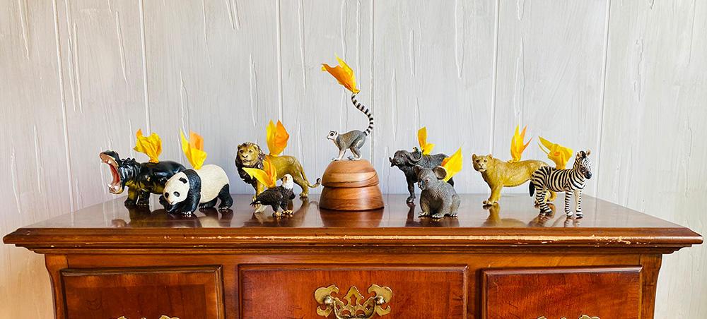 8 toy animals with paper flames attached to them arranged on top of a wood cabinet