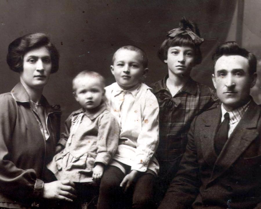 Black and white photograph of a family posing for a portrait. Mother and father sit on either side with three children between them.