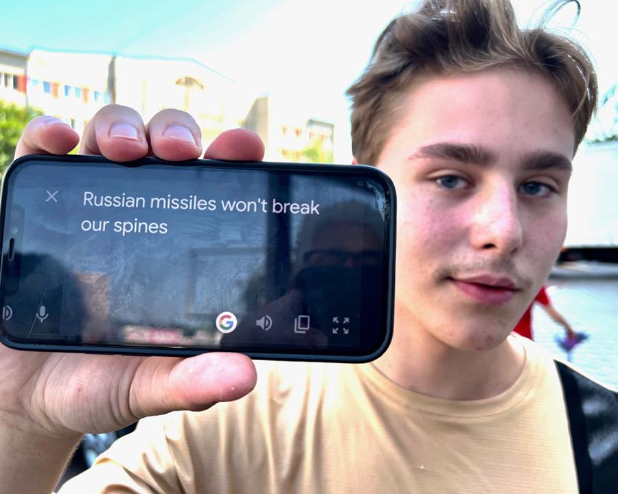 Closeup photograph of a young man outside holding a phone up to show the text, "Russian missiles won't break our spines"