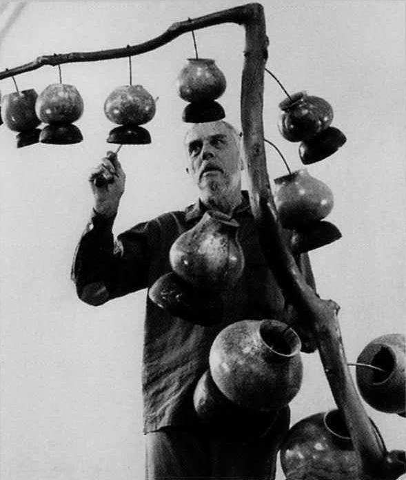 Black and white photo of artist Harry Partch hanging gourds on a branch