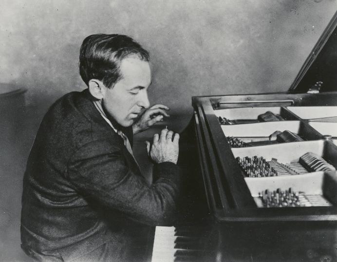 Black and white photo of artist Henry Cowell sitting at his paino