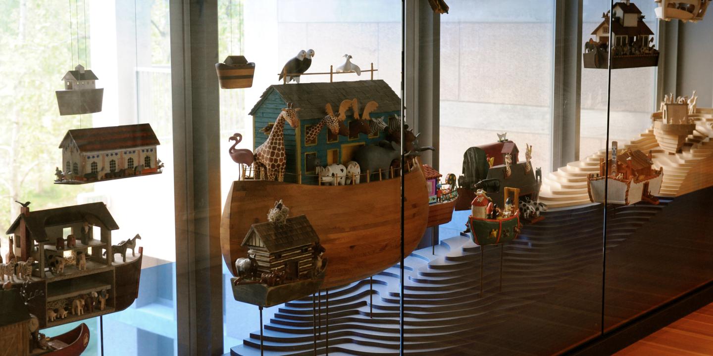 A hallway display of mini wooden ark with tiny animals on them behind glass