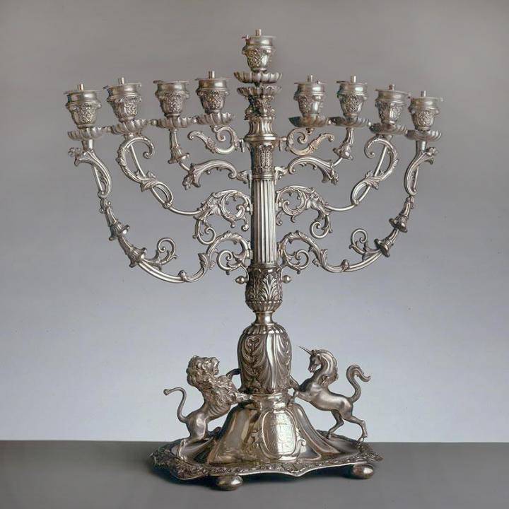 A silver cast Hanukkah lamp with a lion and unicorn at the bottom facing each other. The stems are decorated with ornate leaf foliage. 