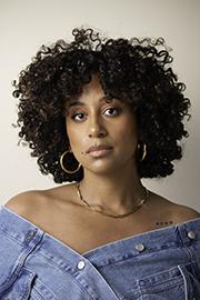 Person with curly black hair, wearing silver hoop earings and an off-the-shoulder denim top