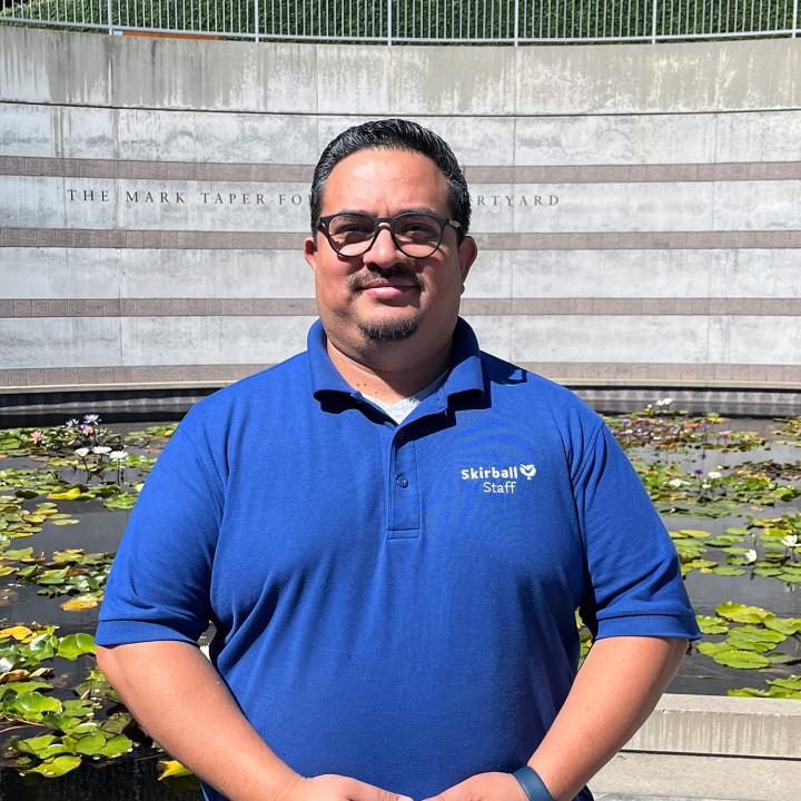 A man smiles outdoors by lily pond.