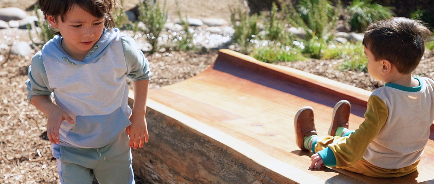 Two kids play outside in a garden.