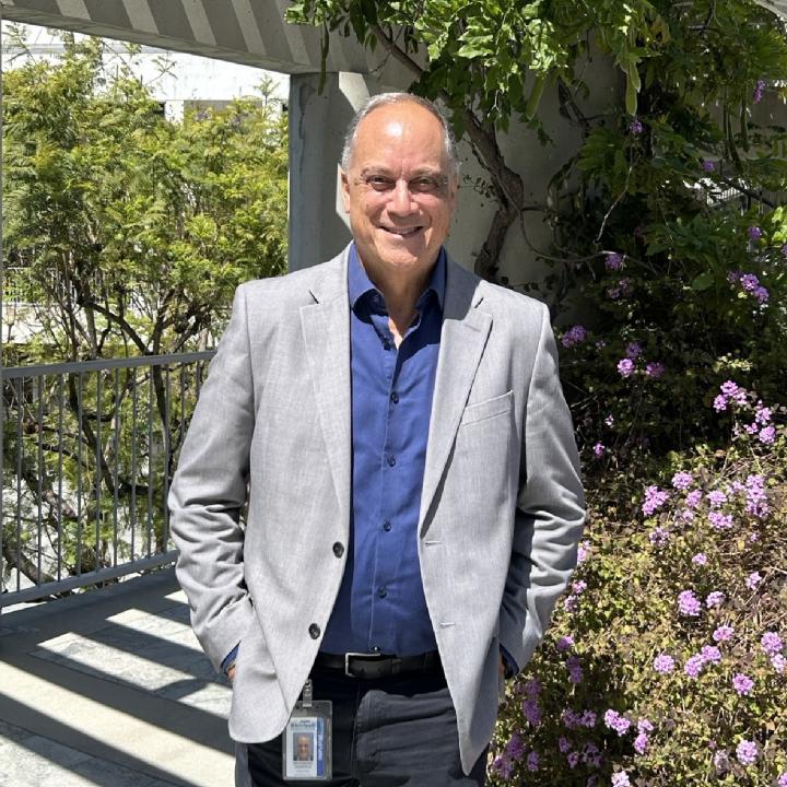 A man in a suit stands next to greenery.