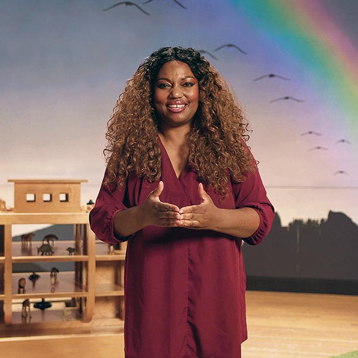 A woman stands in front of a rainbow wall.