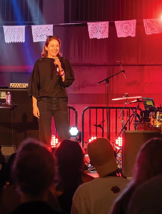 A woman Speaks on an outdoor stage with festive lights and paper banners.