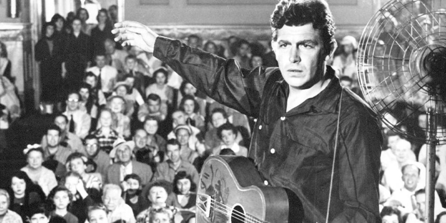 Black and white still from the movie showing the main character on stage in front of a large crowd of fans