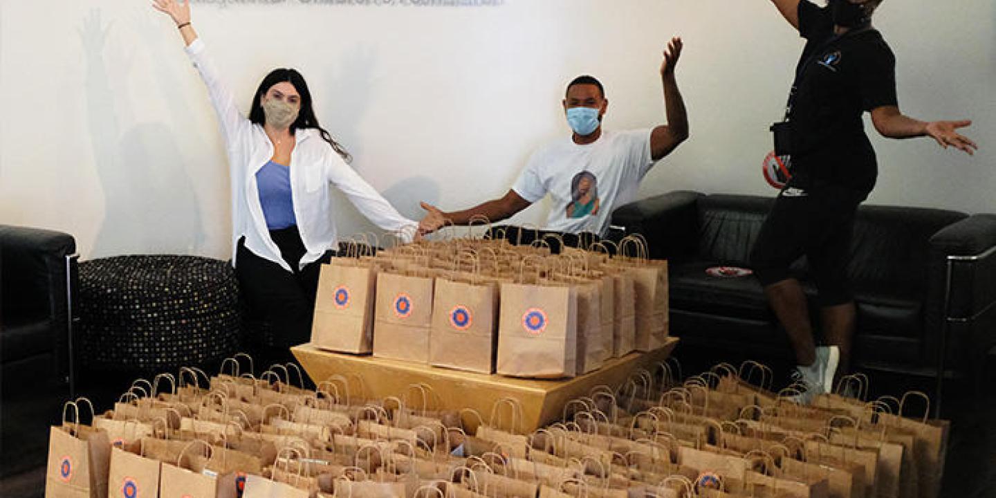 3 people standing next to many bags containing seed planting kits