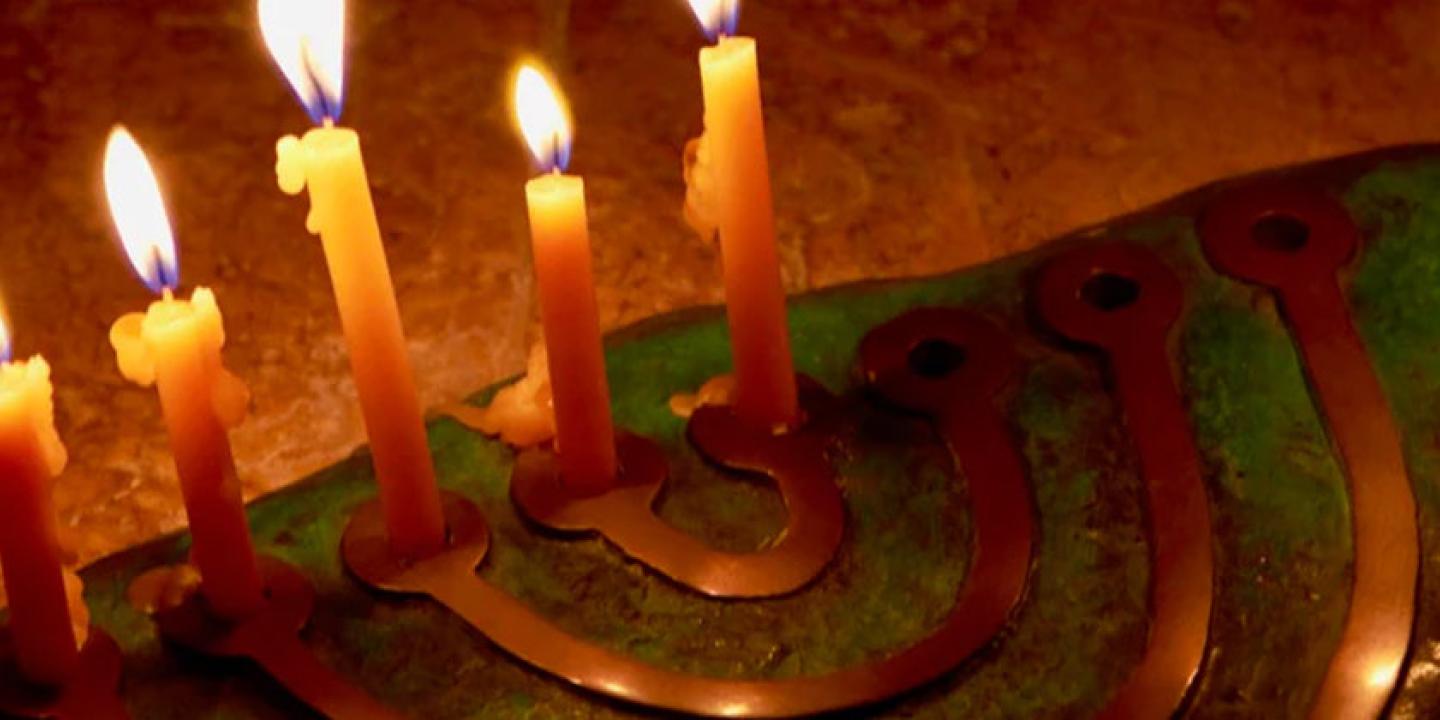 Hanukkah lamp on a flat stone with six, white candles burning